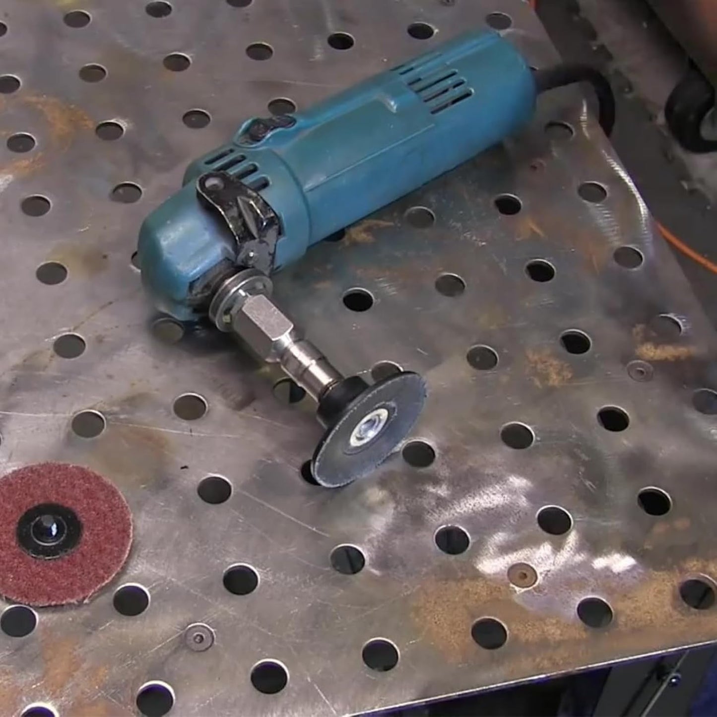 DRILAX angle grinder fitted with flapper adapter and small abrasive flap disc on perforated metal workbench