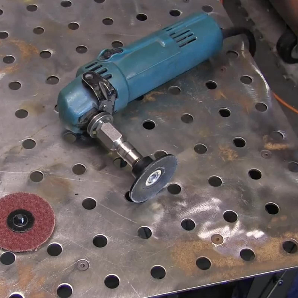 Angle grinder with flapper adapter and surface conditioning disc on a steel table